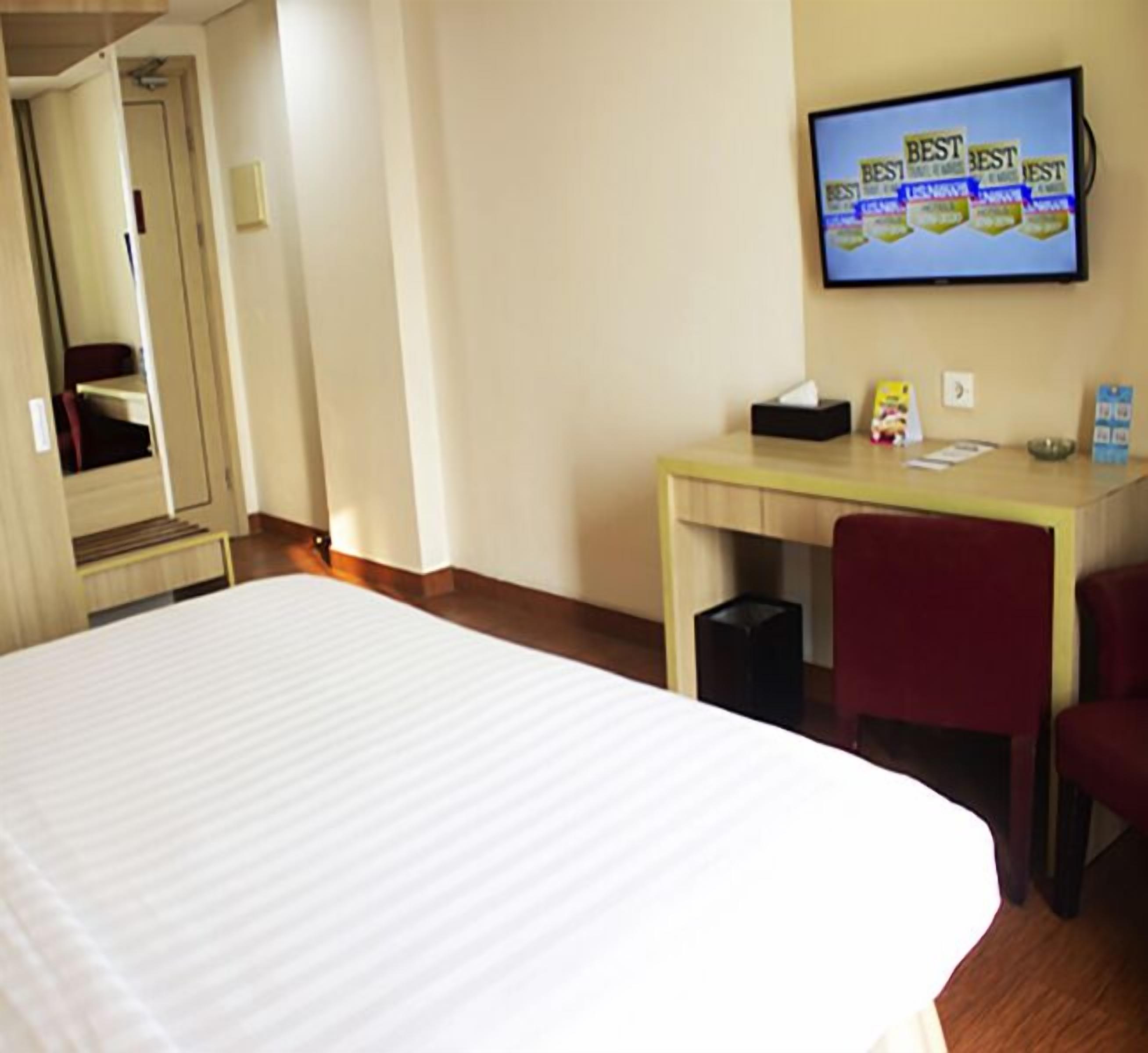 Habitación de hotel con cama, escritorio, silla, televisor y cubo de basura.