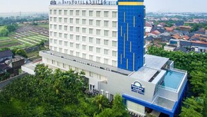 A Days Hotel & Suites building with a prominent blue tower, surrounded by lush greenery and a clear sky.