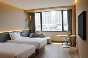 Habitación de hotel con dos camas, una mesita redonda con una silla, un televisor montado en la pared y una ventana con vista a la ciudad.