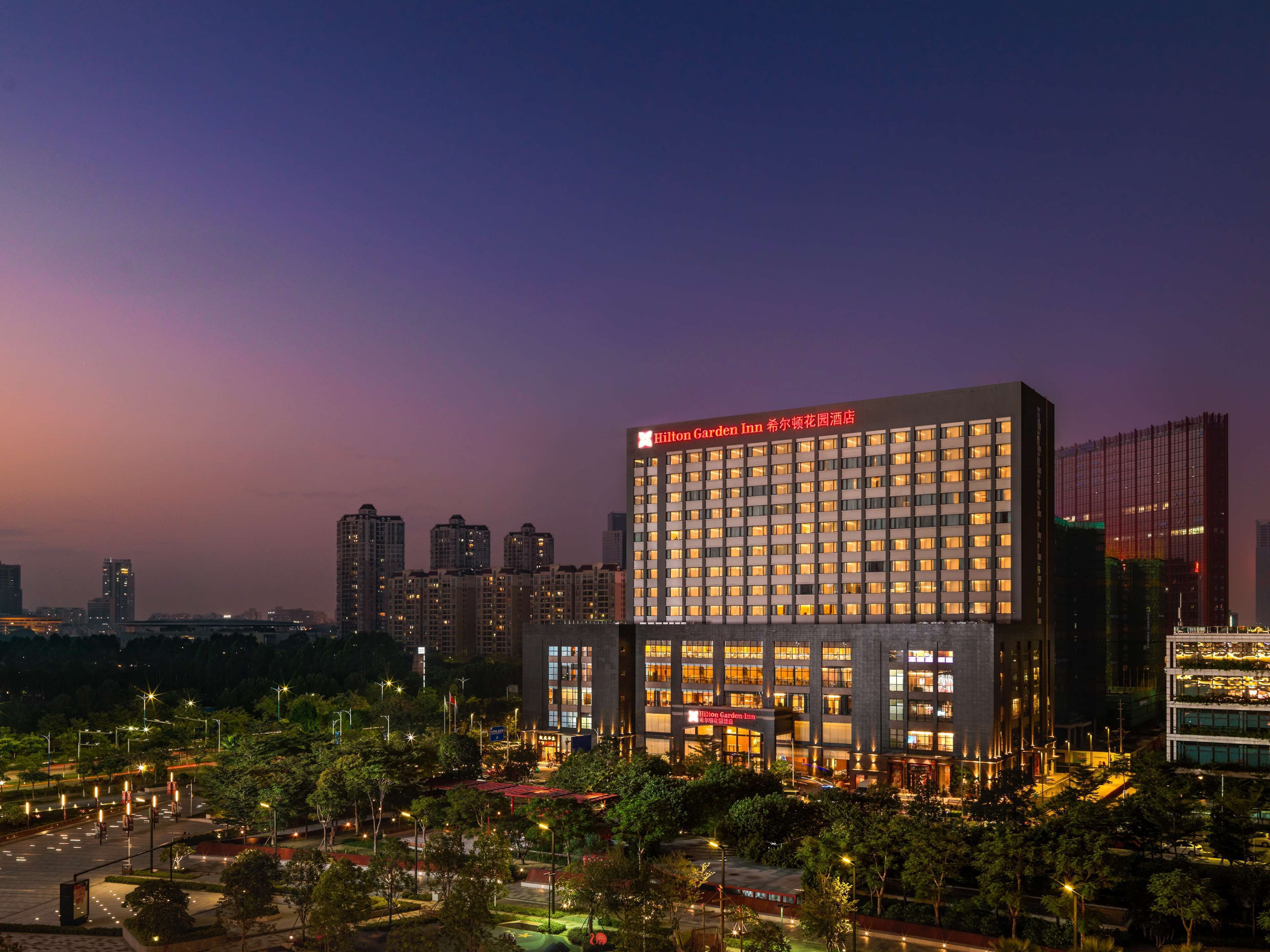 Un moderno edificio de hotel con un letrero llamativo, rodeado de vegetación y otros edificios altos.