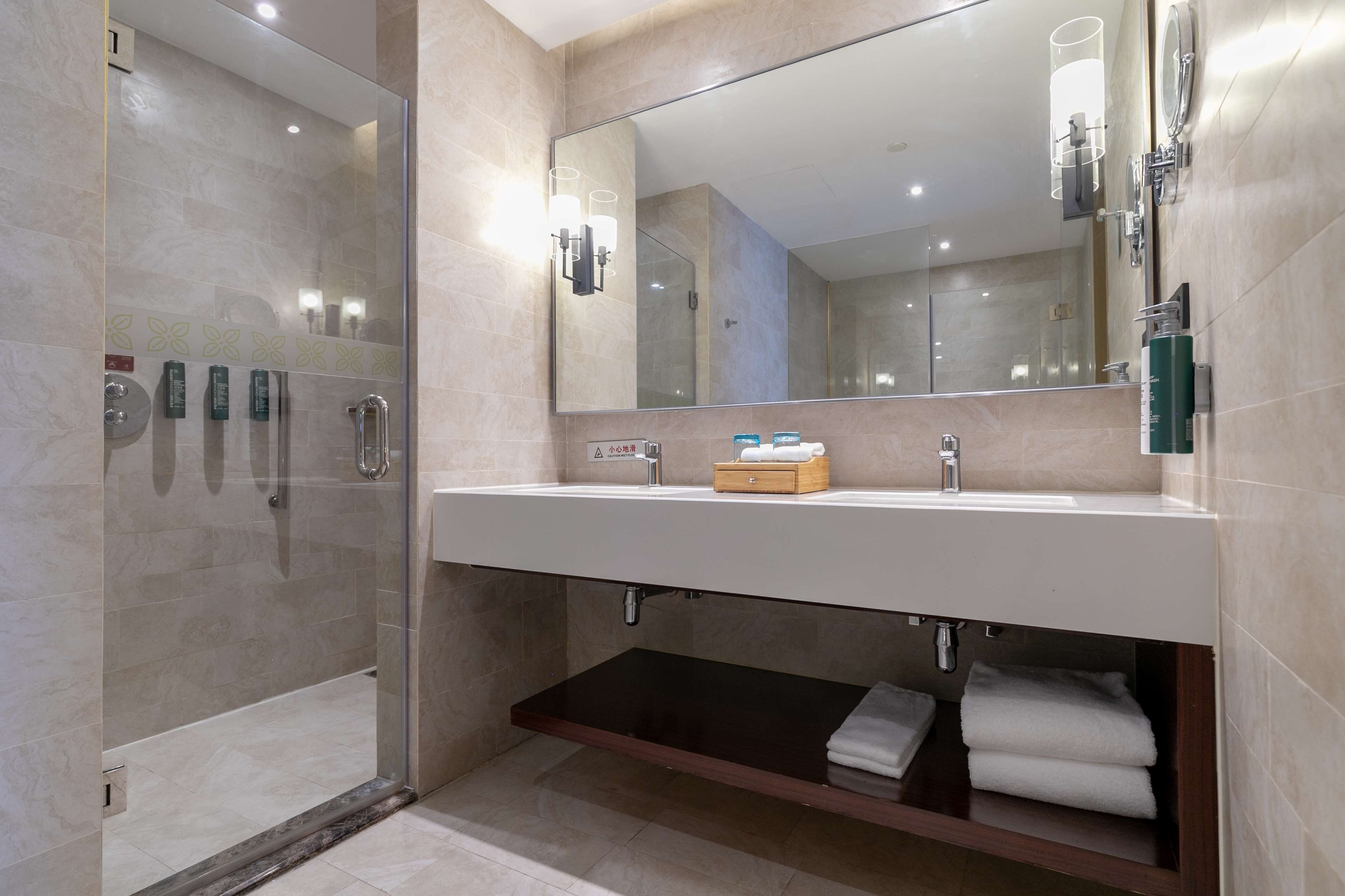 A modern bathroom with a glass shower enclosure, a large mirror, and a vanity with a sink and towel storage.