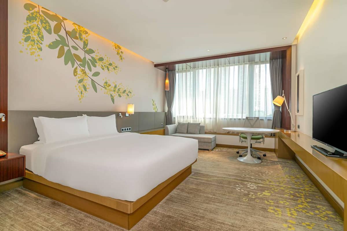 A hotel room with a large bed, a desk, a TV, and a window with curtains.