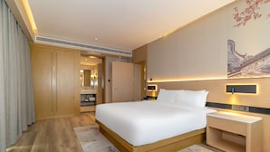 Une chambre d’hôtel moderne avec un grand lit, une armoire en bois, une table de chevet et un tableau au mur.