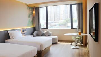 Habitación de hotel con dos camas, una mesita redonda y un ventanal con vistas a la ciudad.
