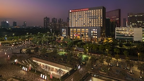 A modern hotel with a prominent red sign, surrounded by a landscaped area with trees and a parking lot. - Hilton Garden Inn Foshan (Foshan)
