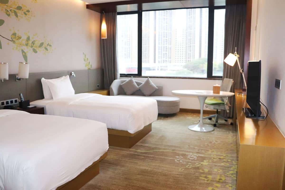 A hotel room with two beds, a sofa, a small table, a lamp, and a TV.