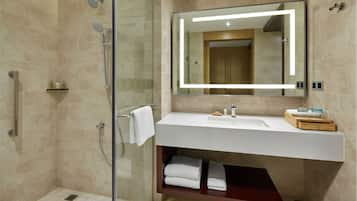 Une salle de bain moderne dotée d’une douche à parois de verre, d’un lavabo blanc et d’un grand miroir avec éclairage intégré.