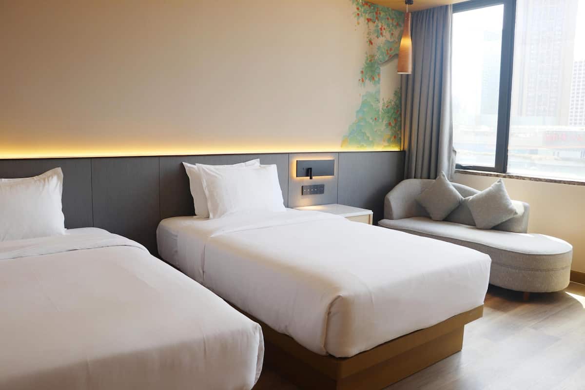 A hotel room with two beds, a sofa, a nightstand, and a window with a city view.