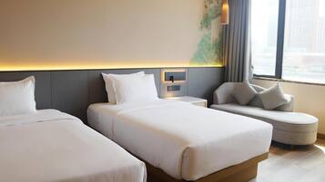 Une chambre d’hôtel avec deux lits, un canapé, une table de chevet et une fenêtre donnant sur la ville.