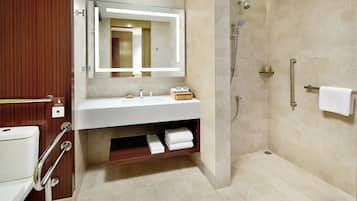 A modern bathroom with a white sink, a large mirror, a shower area, and a wooden vanity.