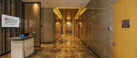 Un moderno vestíbulo de hotel con una recepción, un largo pasillo y una puerta de madera.