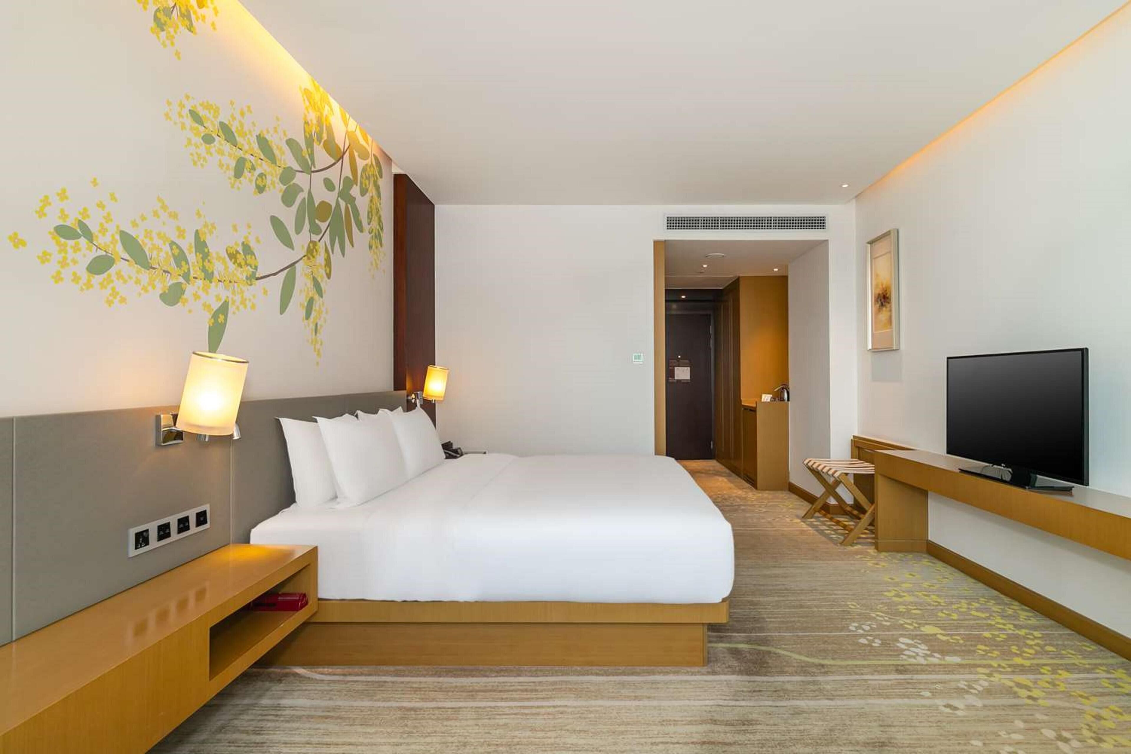 A hotel room with a bed, bedside lamps, a TV, and a small seating area.