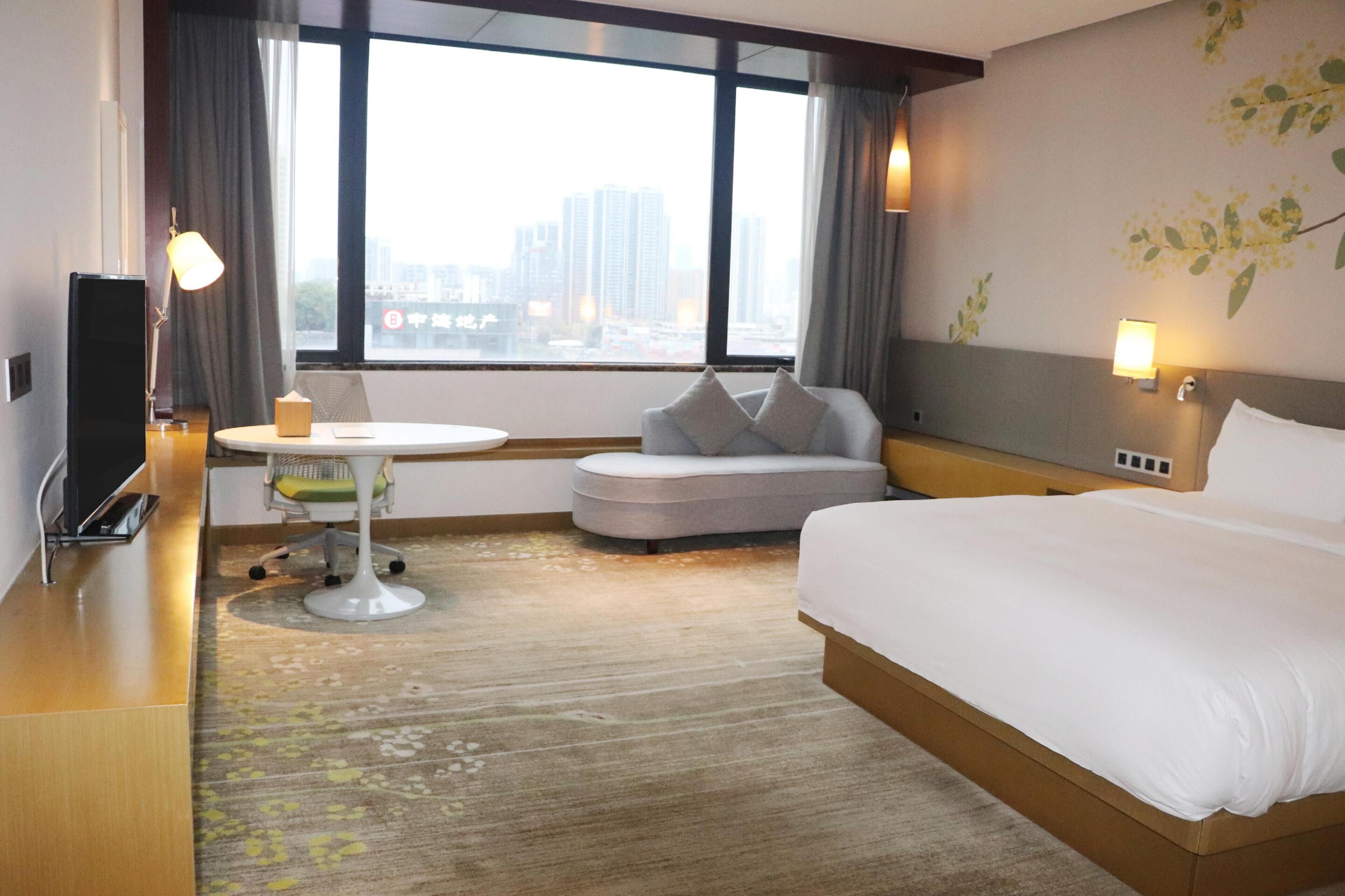 Hotelkamer met een bed, een bureau, een stoel, een klein tafeltje en een raam met uitzicht op de stad.