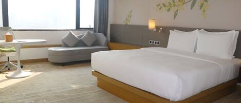 Habitación de hotel con una cama grande, una pequeña mesa redonda, un sofá y una ventana con cortinas.
