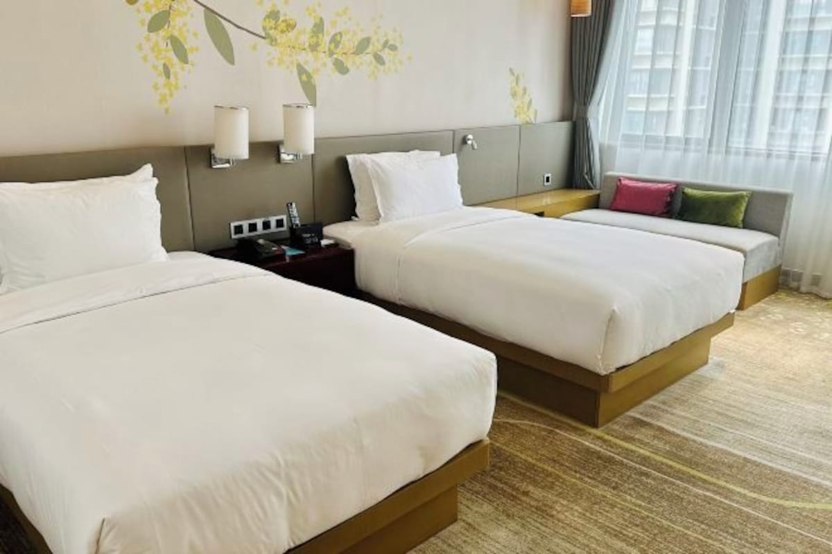 Habitación de hotel con dos camas, una mesita de noche, una lámpara y una ventana con cortinas.