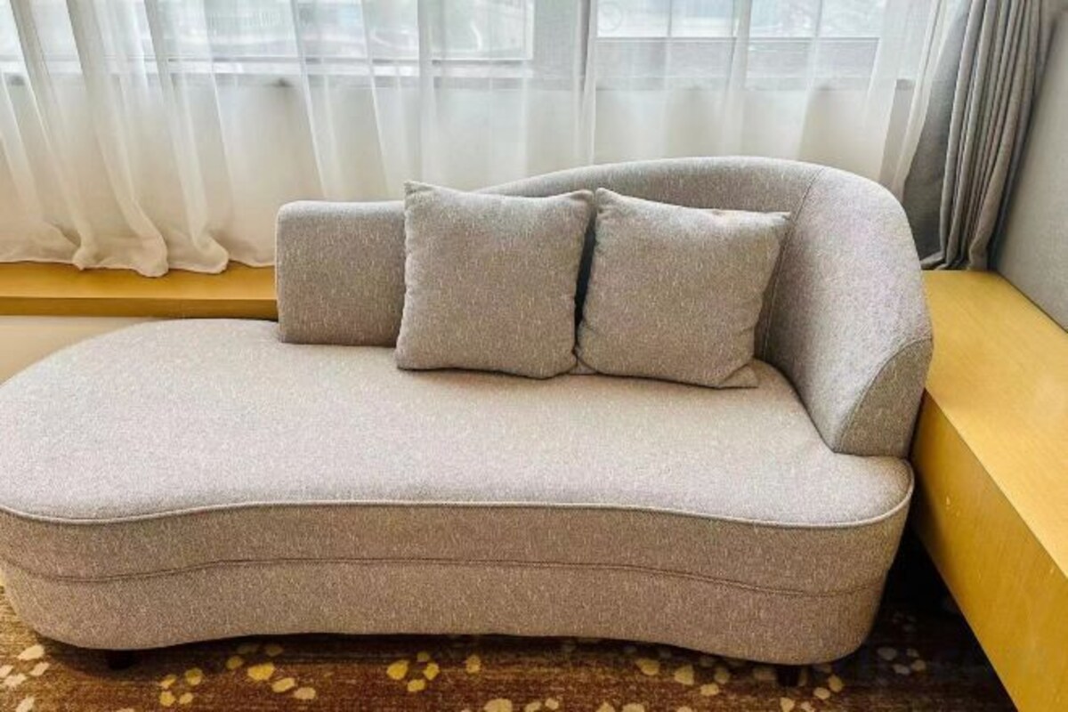 A sofa with a curved design, positioned in a room with a window and curtains.
