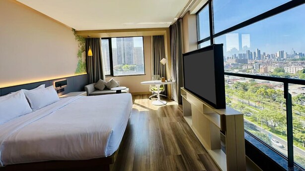 A hotel room with a large bed, a desk, a chair, a TV, and a city view. - Hilton Garden Inn Foshan (Foshan)