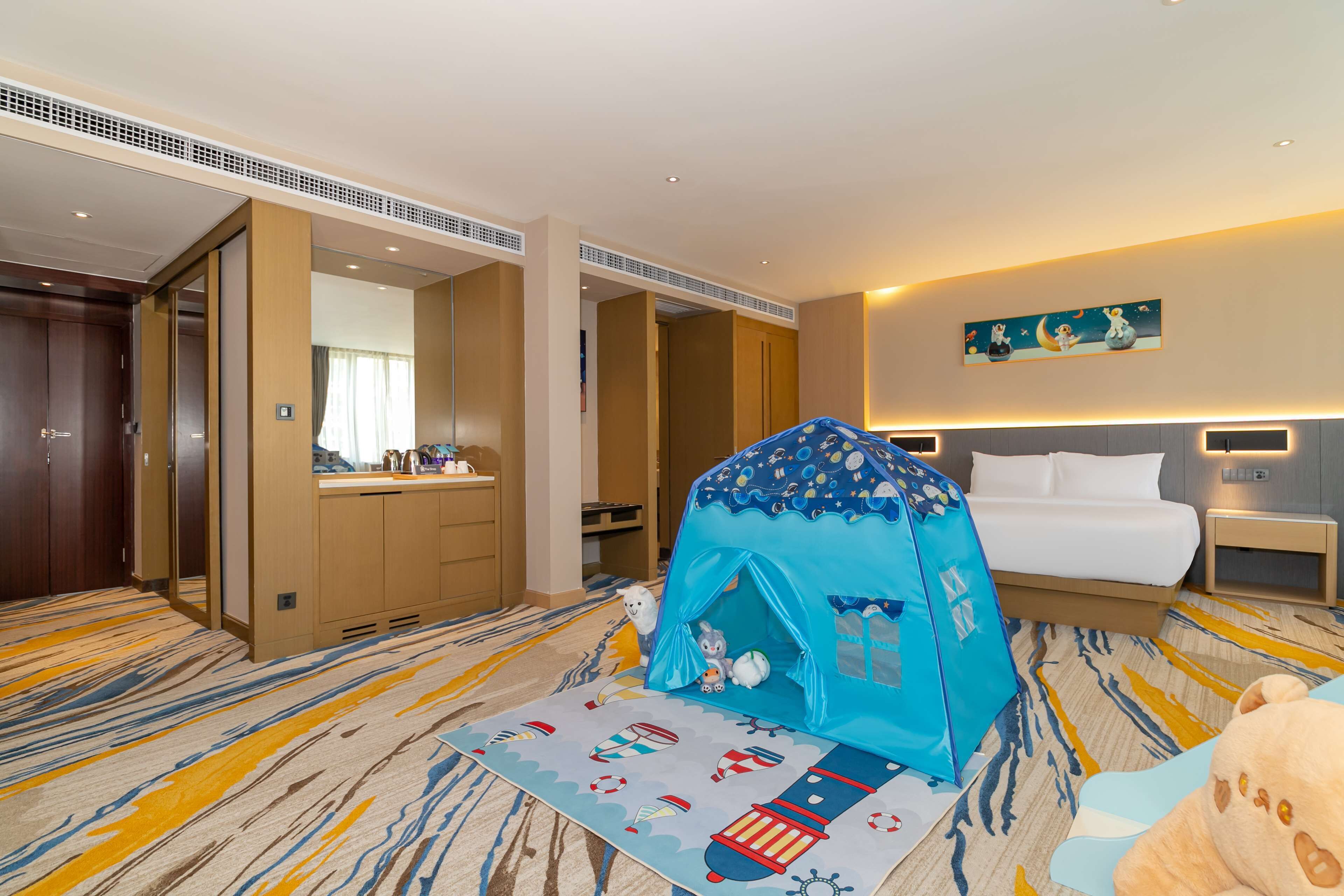 Une chambre d’hôtel avec un grand lit, une tente, un jouet en peluche et une moquette à motifs nautiques.