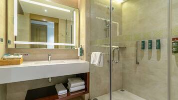 A modern bathroom with a glass-enclosed shower, a large mirror, and a white sink.