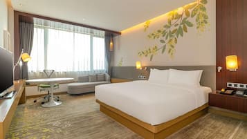 A modern hotel room with a large bed, a sofa, a dining table, and a TV.