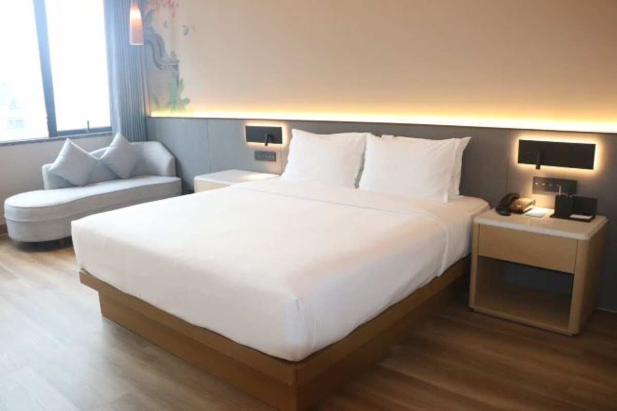 A modern hotel room with a large bed, bedside tables, a sofa, and a view of the outdoors.