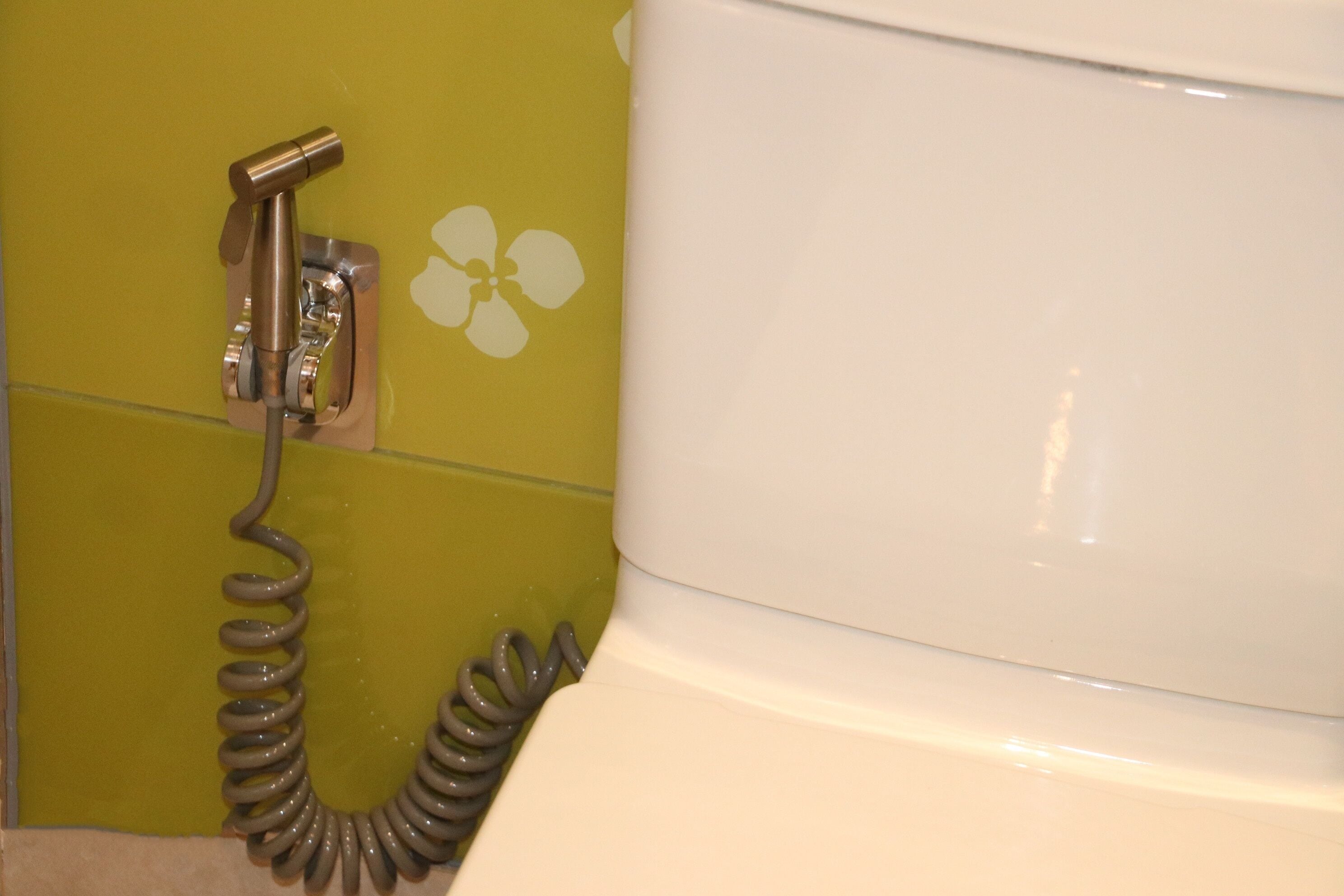 A bathroom with a shower head attached to a wall, a toilet, and a flower decal on the wall.