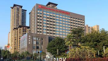 A modern hotel building with a prominent Hilton Garden Inn sign, surrounded by lush greenery and a well-maintained park area.