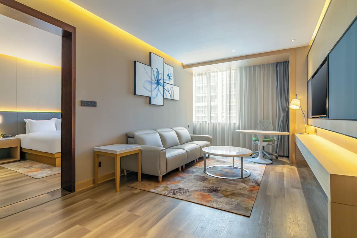 A modern hotel room with a bed, sofa, round coffee table, and a TV.