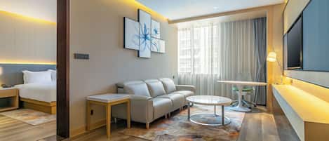 A modern hotel room with a bed, sofa, round coffee table, and a TV.