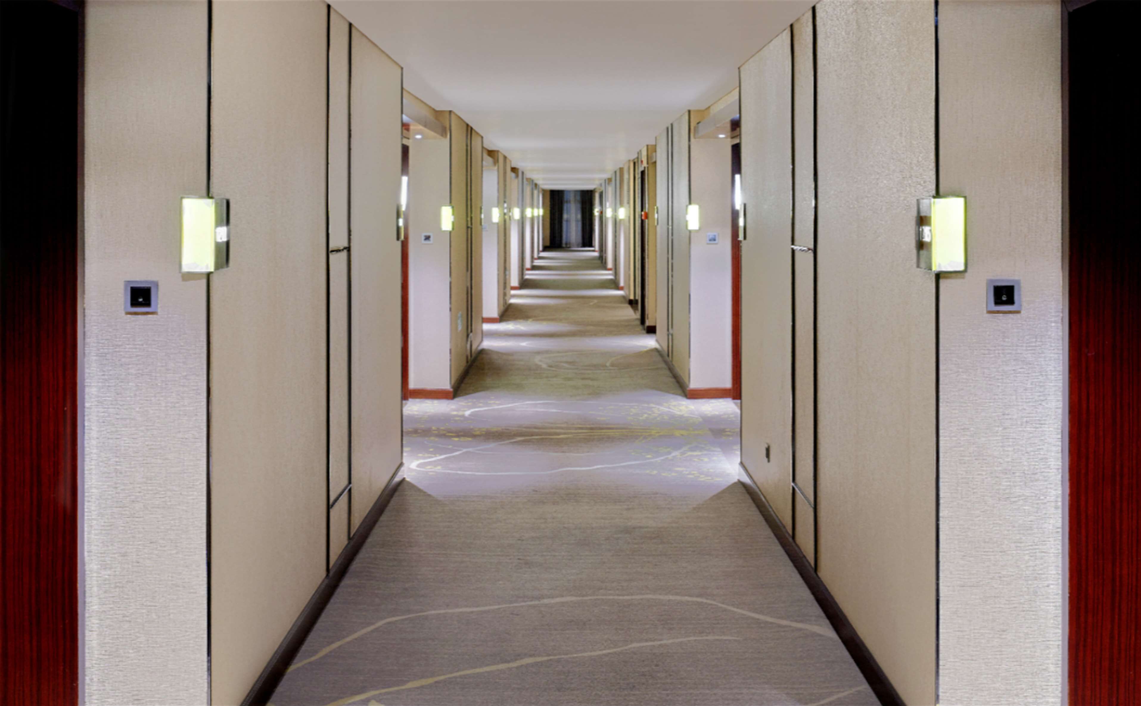 A hotel hallway with multiple rooms on either side, each with a door and a light fixture above it.