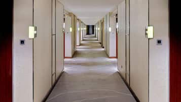 Un pasillo de hotel con varias habitaciones a ambos lados, cada una con una puerta y una lámpara encima.