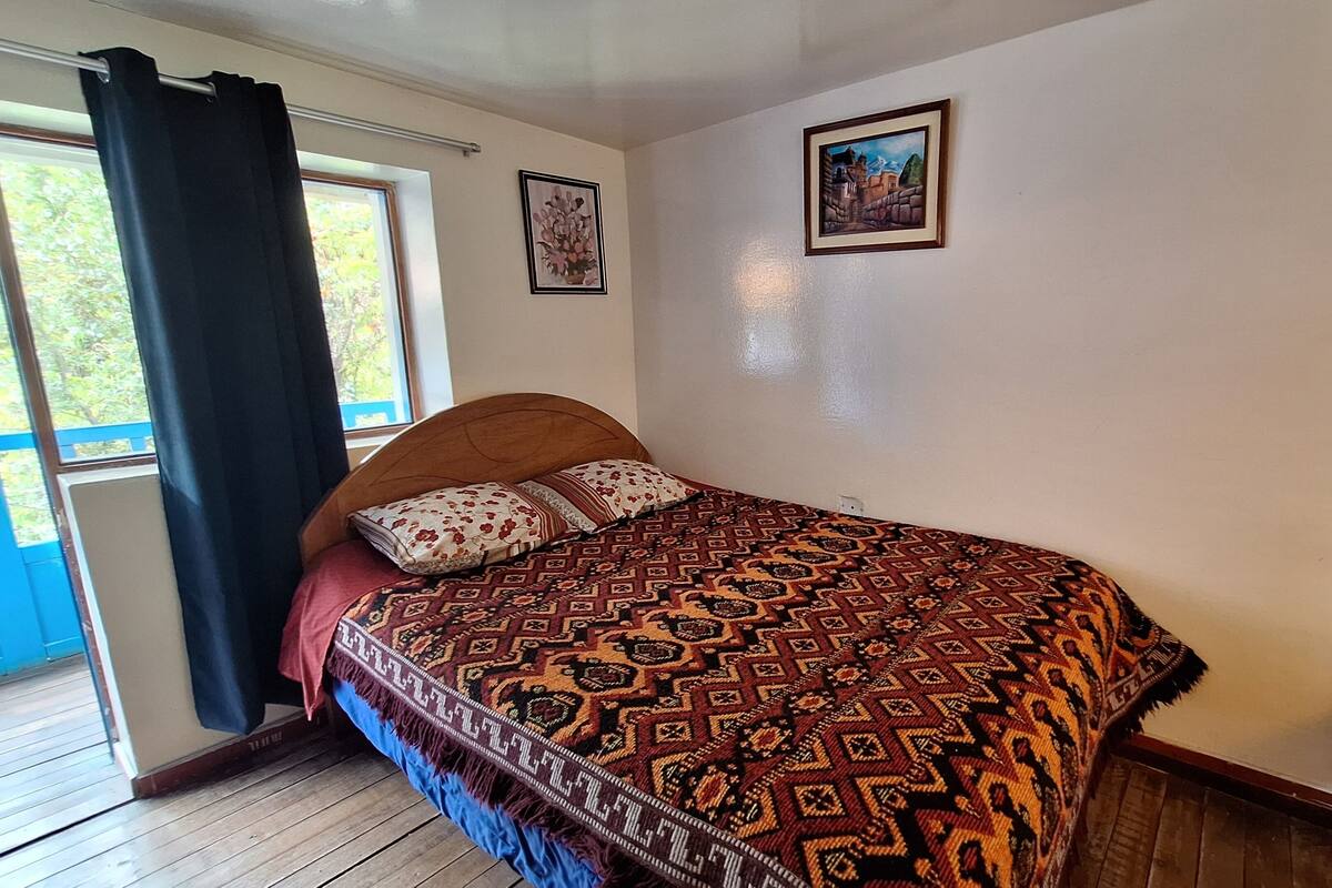 A bedroom with a wooden bed, a window with curtains, and two framed pictures on the wall.