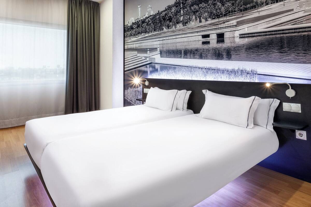 Ein Hotelzimmer mit einem großen Bett, Blick auf einen Fluss und einem Wandbild einer Brücke.
