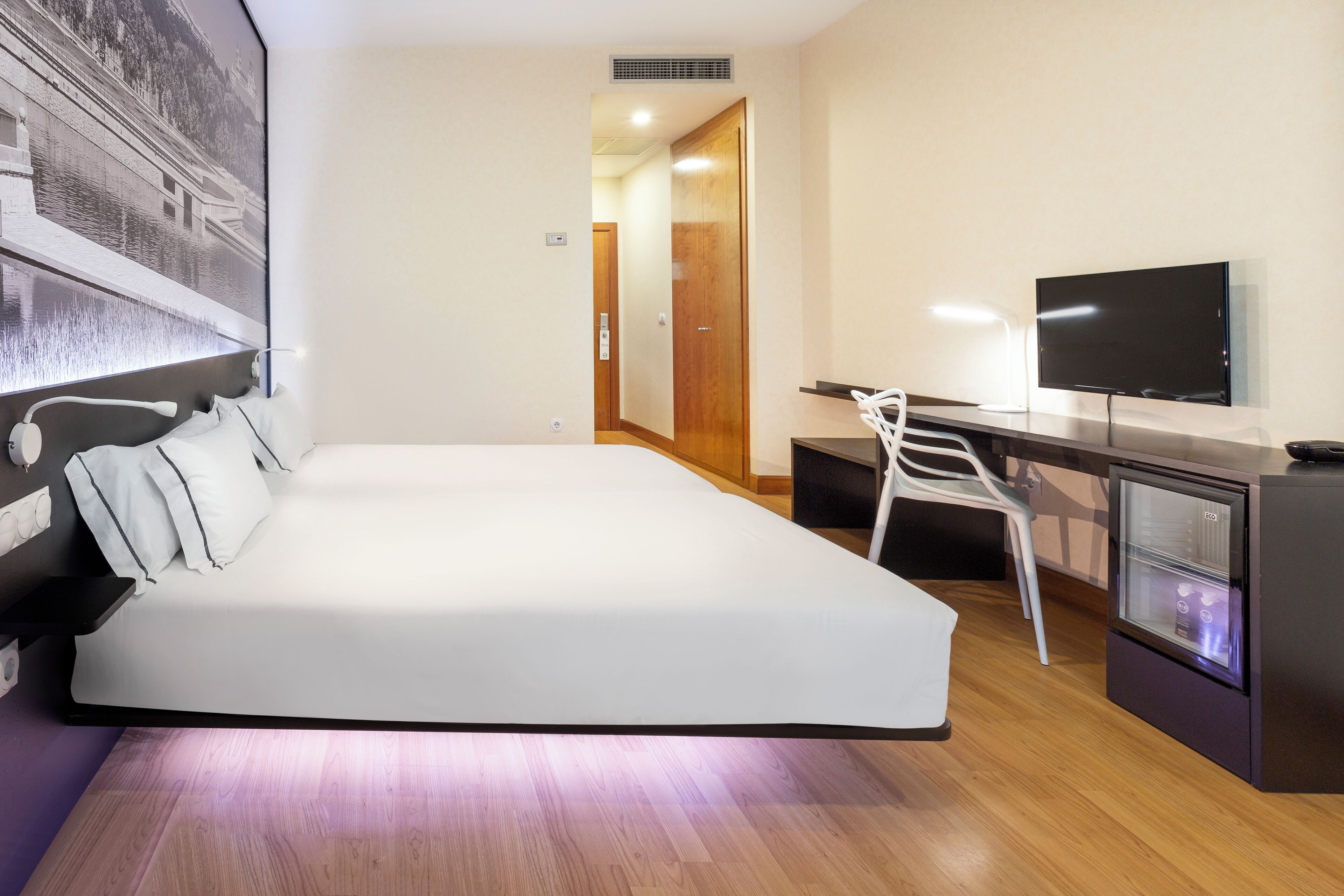 Een moderne hotelkamer met een bed, een bureau, een televisie en een koelkast.
