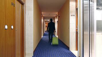 A hotel hallway with doors numbered 912 and 901, a blue patterned carpet, and a person with a green suitcase.