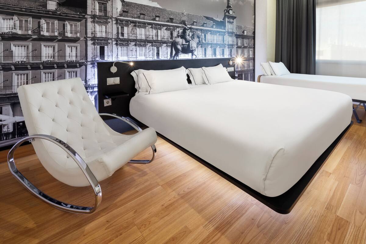 Ein Schlafzimmer mit einem großen Bett, einem weißen Polsterstuhl und einem Wandgemälde eines Gebäudes.