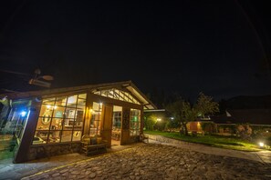 A stone-floored building with large windows and a covered porch, surrounded by a well-maintained lawn and trees. - Andean Wings Valley (Urubamba)
