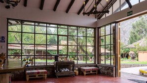 A spacious room with large windows, a wooden bench, and a rustic chandelier. - Andean Wings Valley (Urubamba)