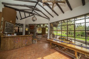 Un interior rústico con vigas de madera a la vista, una chimenea de piedra y un ventanal con vistas al exterior.