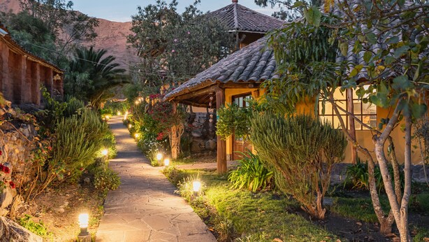 A stone pathway flanked by lush greenery and small structures with tiled roofs. - Andean Wings Valley (Urubamba)
