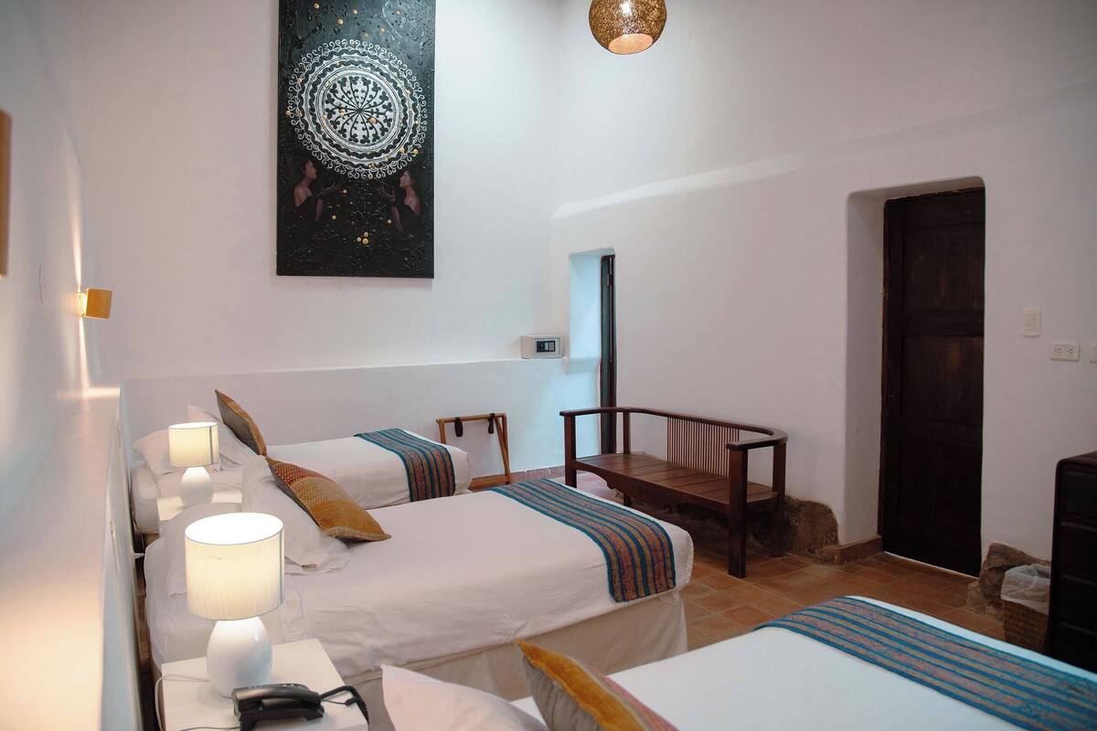 A hotel room with two beds, a desk, a chair, a wall-mounted artwork, and a door.