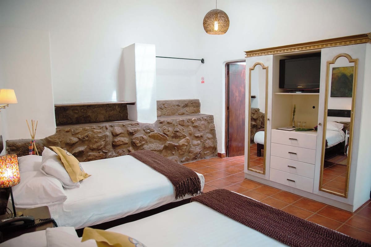 A bedroom with two beds, a stone wall, a wardrobe with a mirror, and a television.