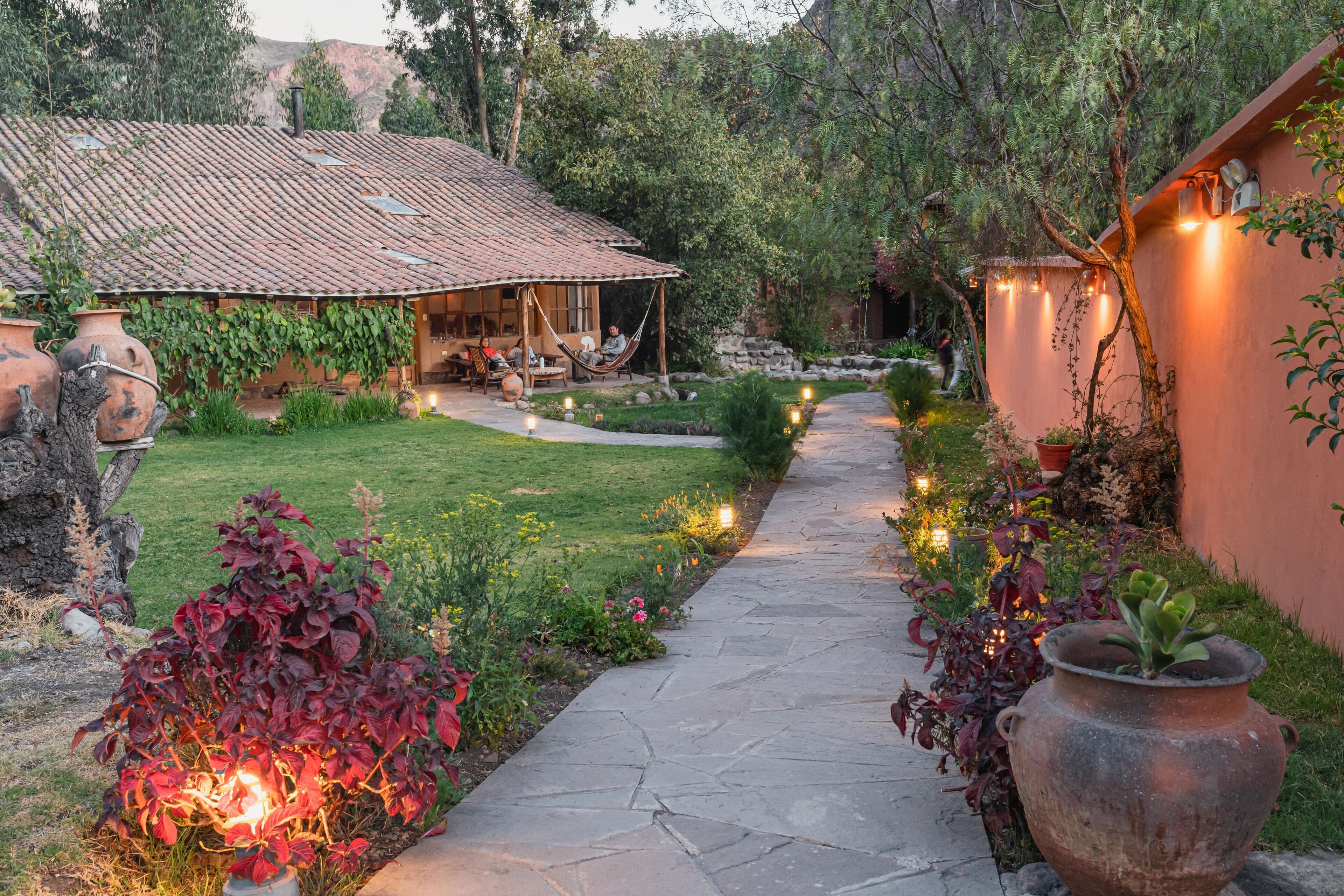 A rustic outdoor area with a stone pathway, potted plants, and a small seating area under a tiled roof.