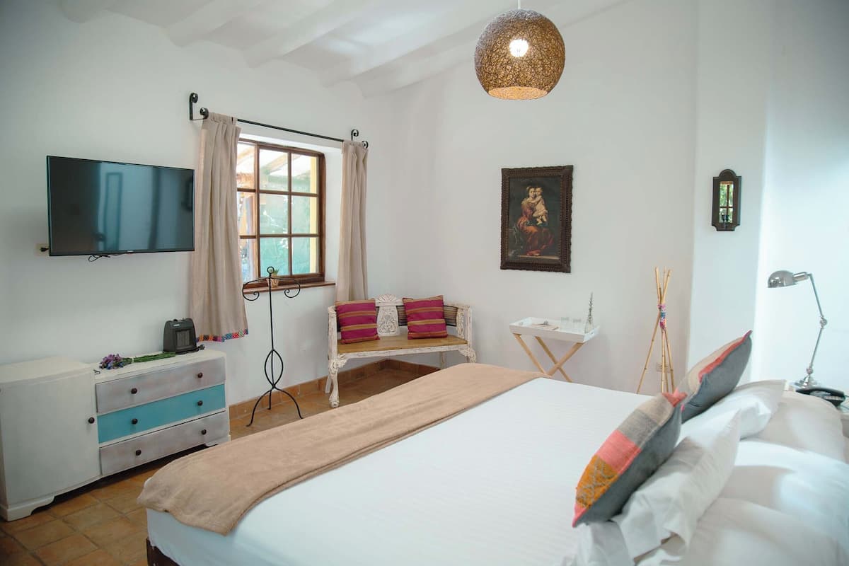 A bedroom with a bed, a TV, a desk, and a window with curtains.
