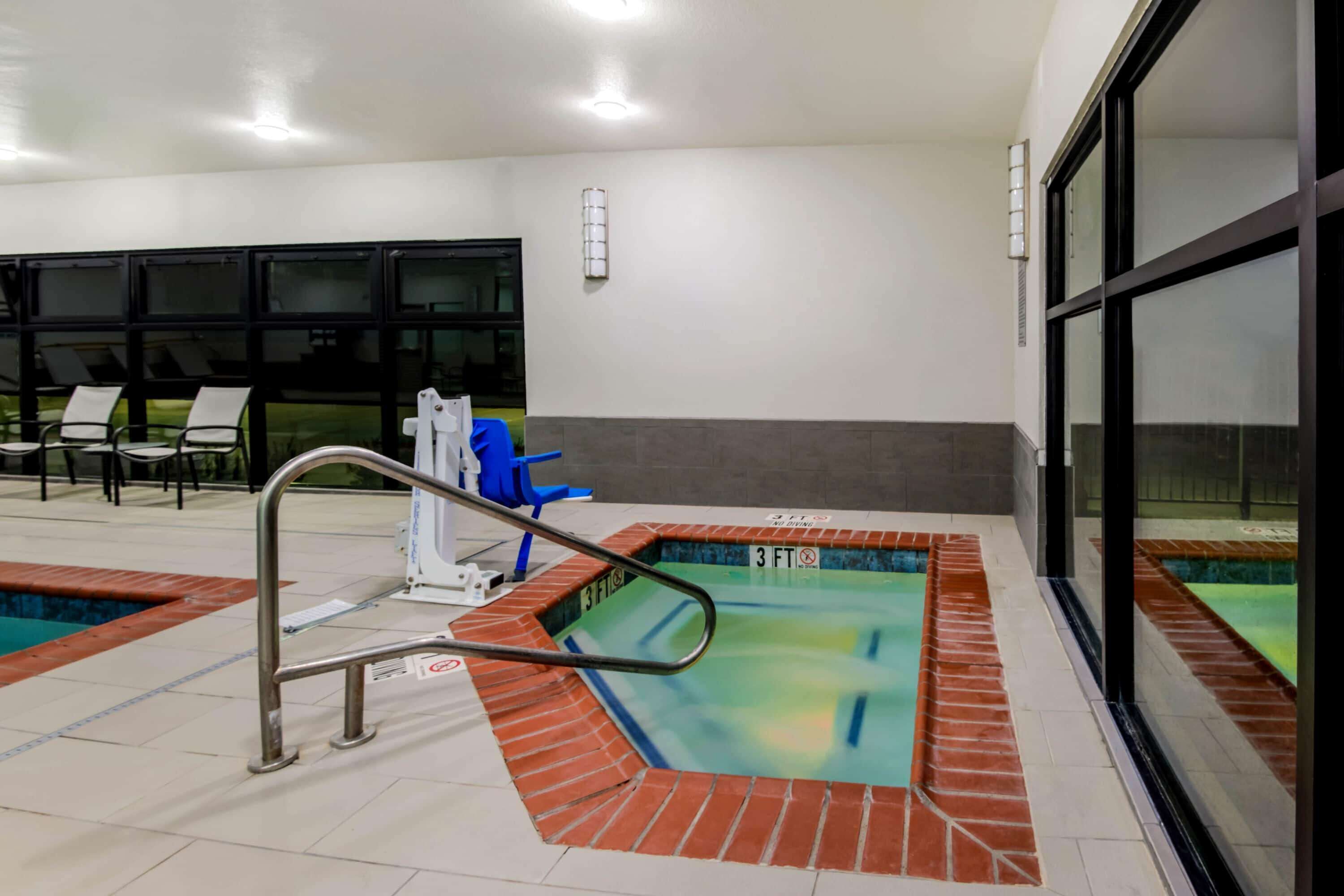 An indoor swimming pool with a metal ladder, lounge chairs, and a blue chair near the pool.