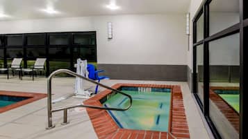 An indoor swimming pool with a metal ladder, lounge chairs, and a blue chair near the pool.