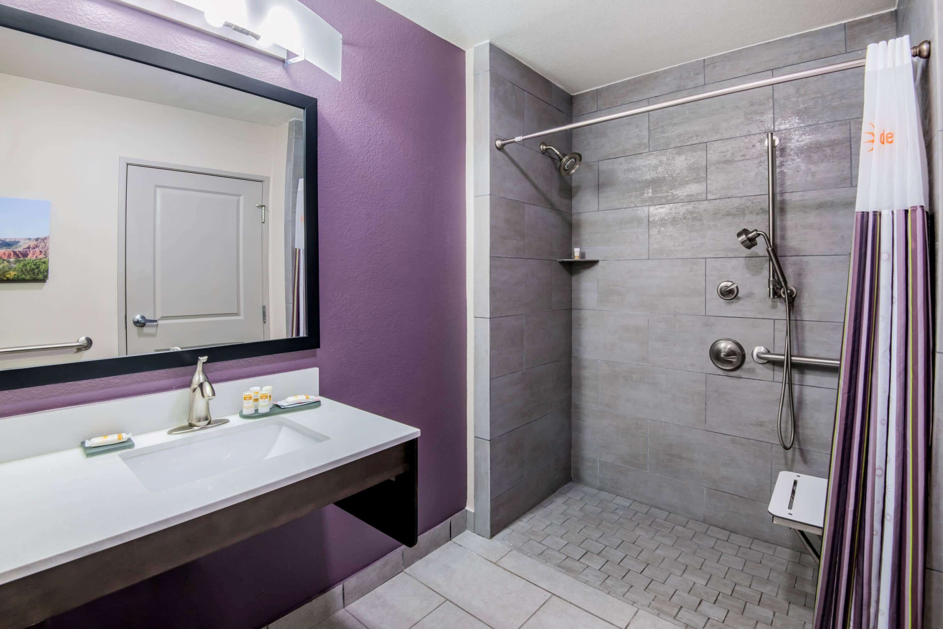 A bathroom with a white sink, purple walls, a shower with a glass door, and a mirror above the sink.