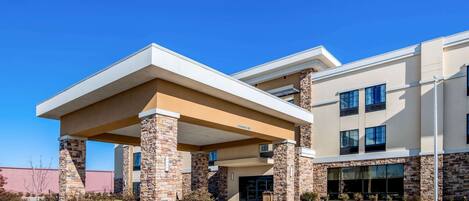 A modern building with a covered entrance, stone pillars, and a clear blue sky.