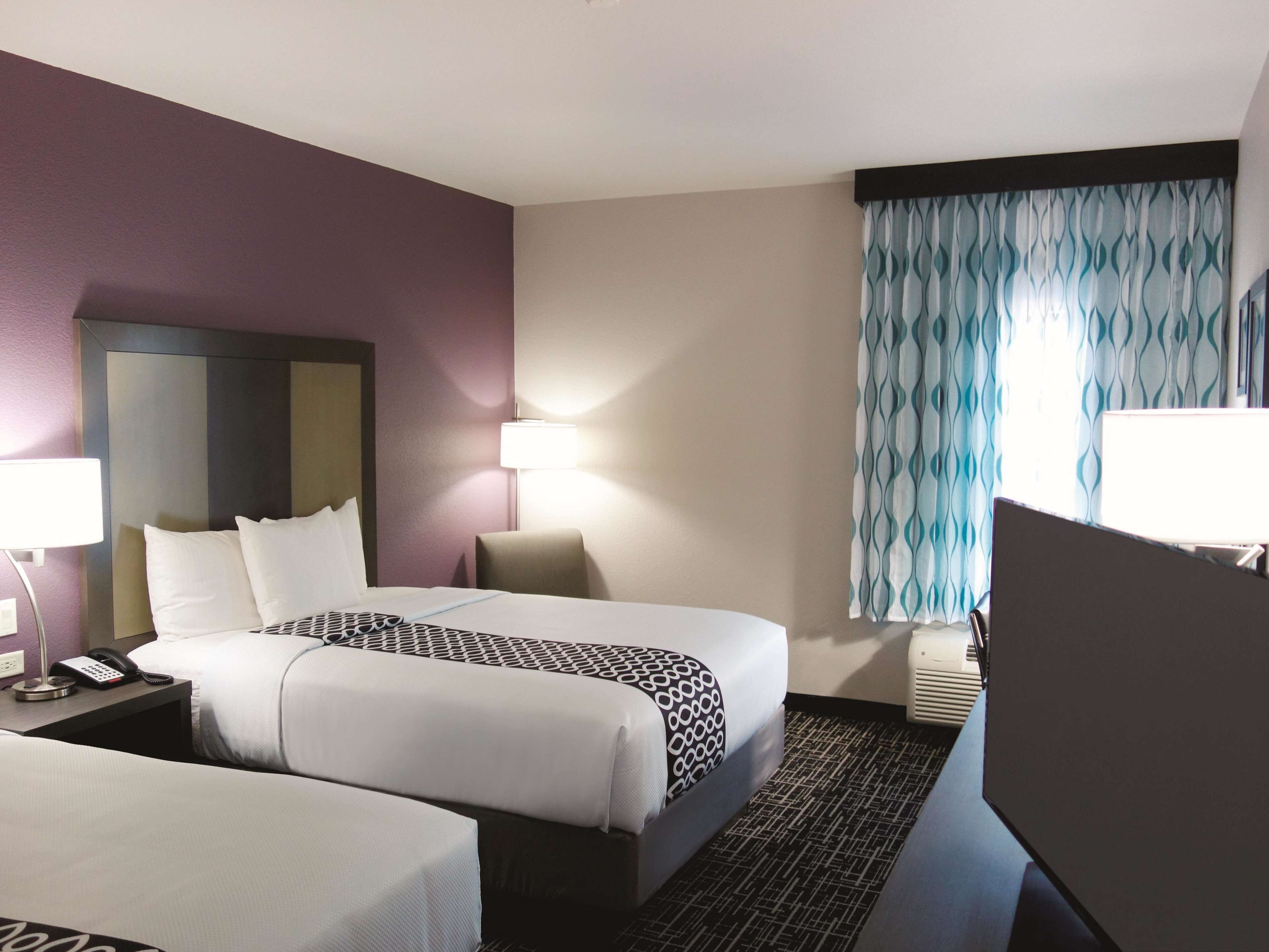 Habitación de hotel con dos camas, un escritorio, una silla, una lámpara de escritorio, un teléfono y una ventana con cortinas.