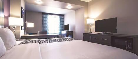 A hotel room with a large bed, a desk with a computer, a television, and a microwave.